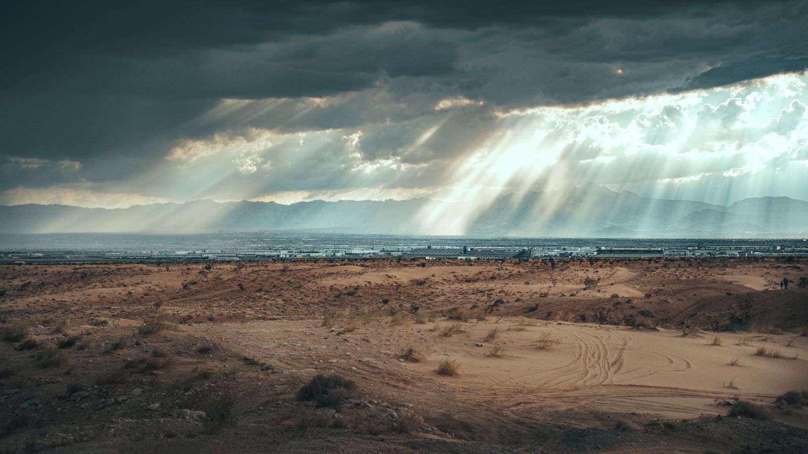 Sunbeams breaking through a heavy storm over a desert plain and distant mountains